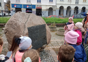 Uczniowi klasy IIa i IIIa stoją przed pomnikiem upamiętniającym nadanie praw miejskich Łodzi, który znajduje się na rynku Starego Miasta. Dzieci czytają tekst z pamiątkowej tablicy.